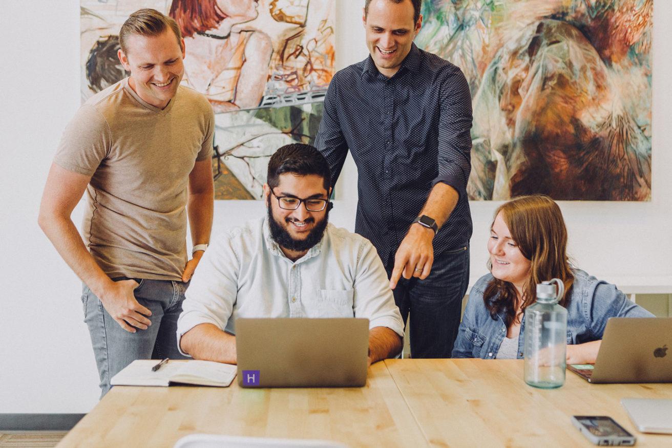 four people looking at a laptop screen